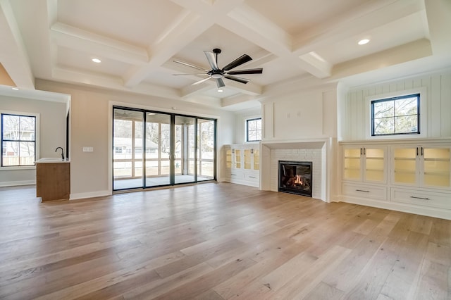 unfurnished living room featuring light wood-type flooring, a brick fireplace, coffered ceiling, and beamed ceiling