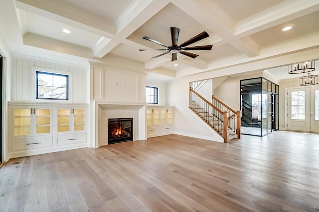 unfurnished living room featuring stairs, plenty of natural light, a glass covered fireplace, and light wood-style floors