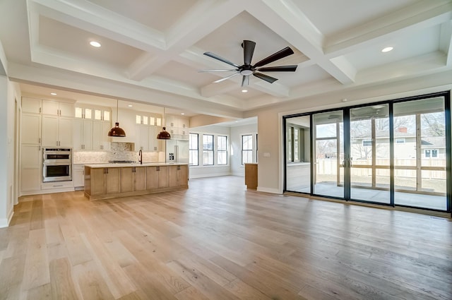 unfurnished living room with beam ceiling, light wood finished floors, a sink, coffered ceiling, and baseboards