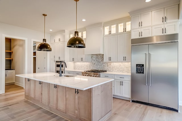 kitchen with light wood finished floors, backsplash, appliances with stainless steel finishes, wall chimney range hood, and light stone countertops