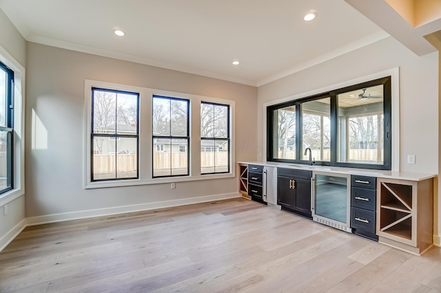 bar featuring wine cooler, ornamental molding, a sink, light wood-type flooring, and baseboards