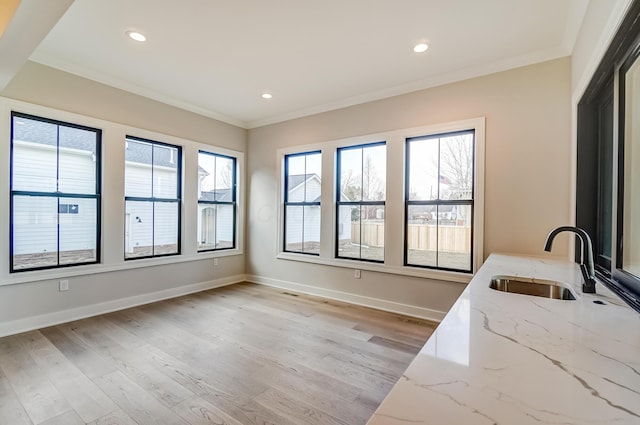 kitchen featuring baseboards, light wood finished floors, a sink, and crown molding