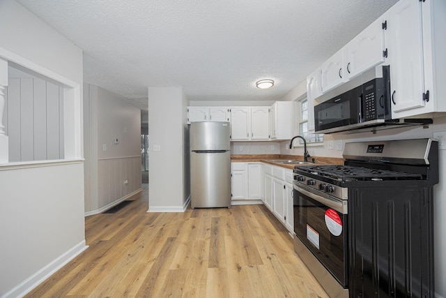 kitchen with appliances with stainless steel finishes, a textured ceiling, sink, light hardwood / wood-style floors, and white cabinetry