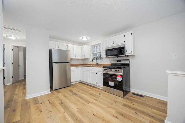 kitchen featuring white cabinets, appliances with stainless steel finishes, a textured ceiling, and light hardwood / wood-style flooring