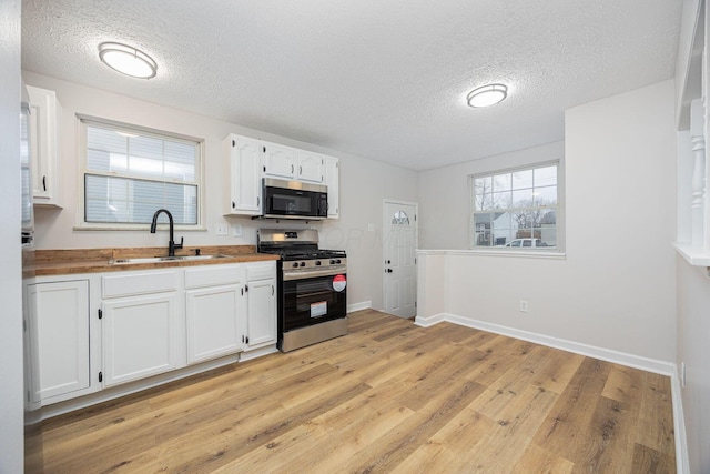 kitchen with butcher block counters, white cabinetry, sink, stainless steel appliances, and light hardwood / wood-style floors