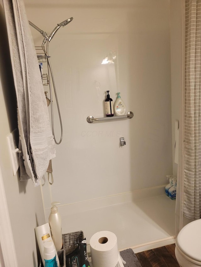 bathroom with hardwood / wood-style flooring, toilet, and curtained shower