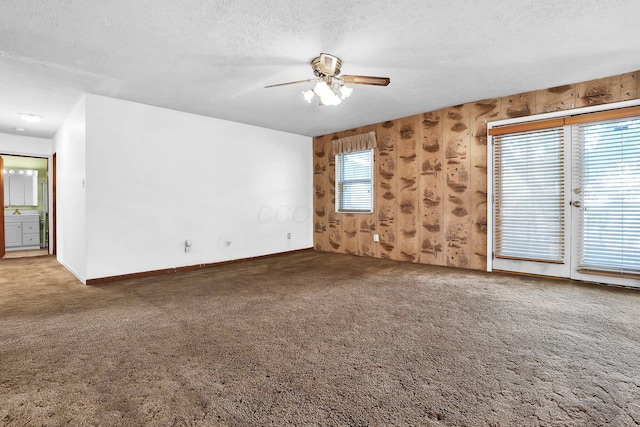 carpeted spare room with ceiling fan, plenty of natural light, a textured ceiling, and wooden walls