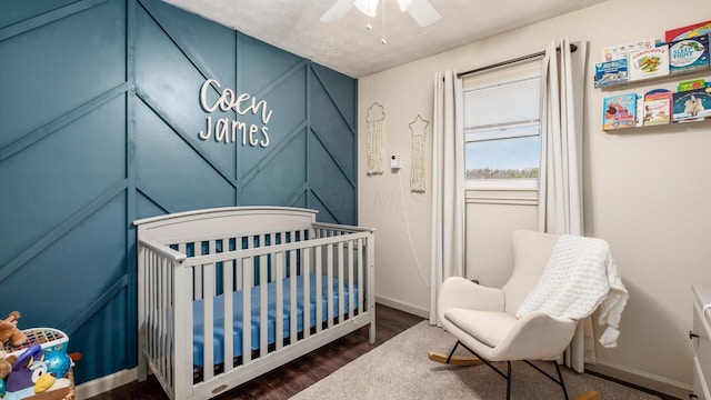 bedroom with a crib, a textured ceiling, ceiling fan, and dark wood-type flooring