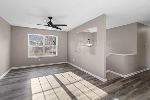 spare room featuring ceiling fan with notable chandelier and dark wood-type flooring