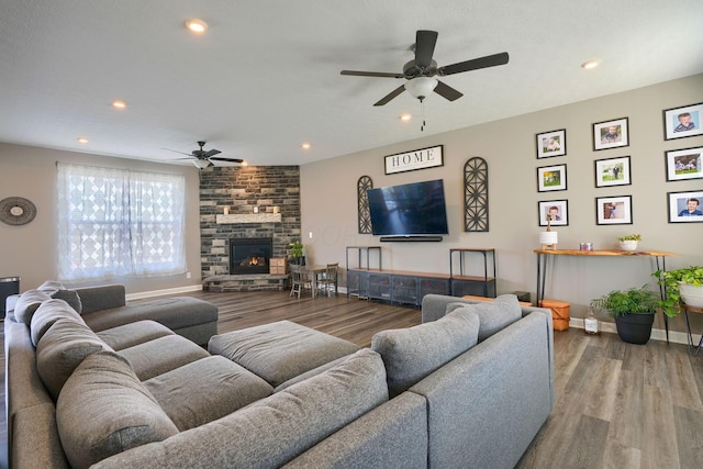 living room with wood-type flooring, a stone fireplace, and ceiling fan