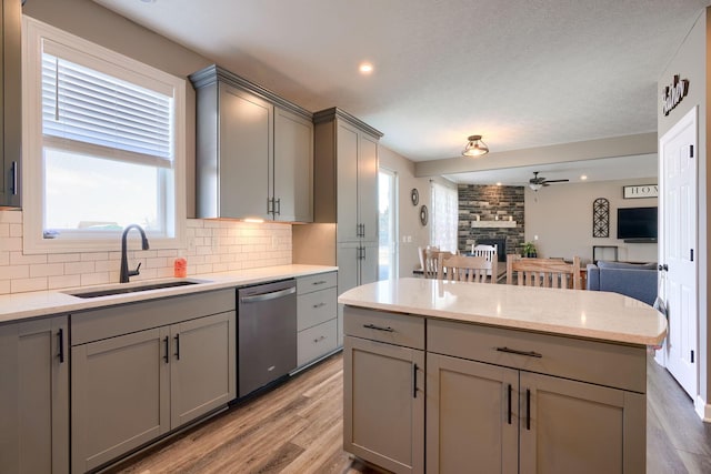 kitchen featuring gray cabinets, a stone fireplace, sink, decorative backsplash, and stainless steel dishwasher