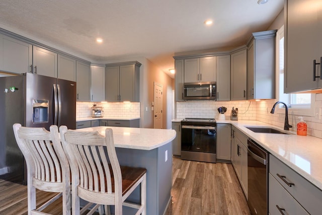 kitchen featuring stainless steel appliances, sink, a breakfast bar, and gray cabinetry