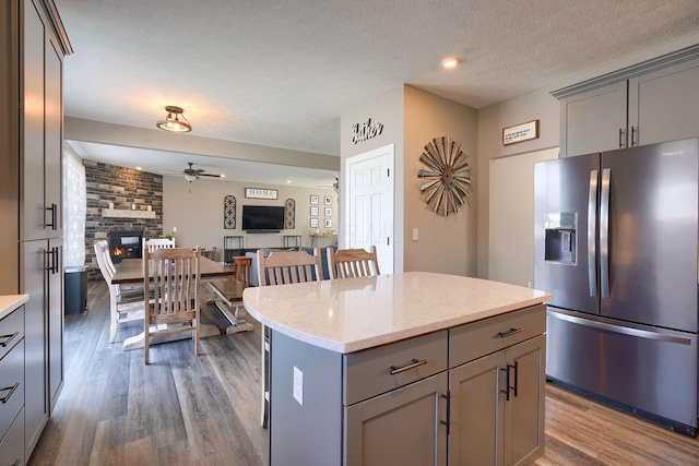 kitchen with a stone fireplace, gray cabinetry, stainless steel fridge, a center island, and ceiling fan