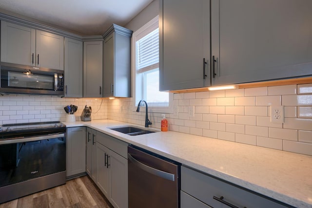 kitchen with sink, gray cabinetry, tasteful backsplash, light hardwood / wood-style flooring, and stainless steel appliances