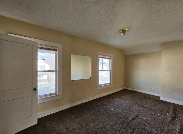 empty room with dark colored carpet, a healthy amount of sunlight, and a textured ceiling