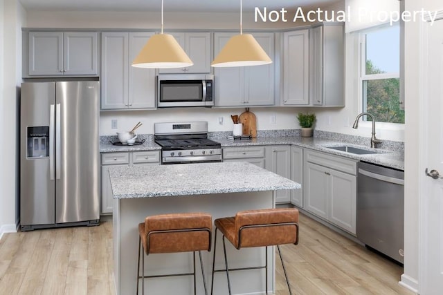 kitchen with appliances with stainless steel finishes, gray cabinets, a sink, and light wood-style flooring