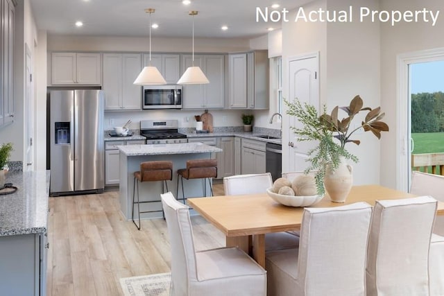 kitchen with light wood-style flooring, a kitchen island, light stone counters, stainless steel appliances, and gray cabinetry