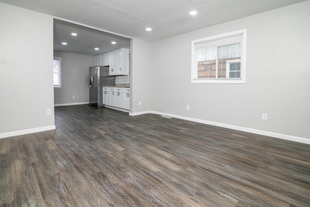 unfurnished living room featuring a textured ceiling, a healthy amount of sunlight, and dark wood-type flooring