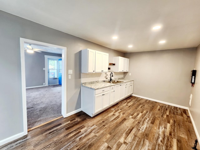 kitchen with white cabinets, light stone counters, sink, and hardwood / wood-style flooring