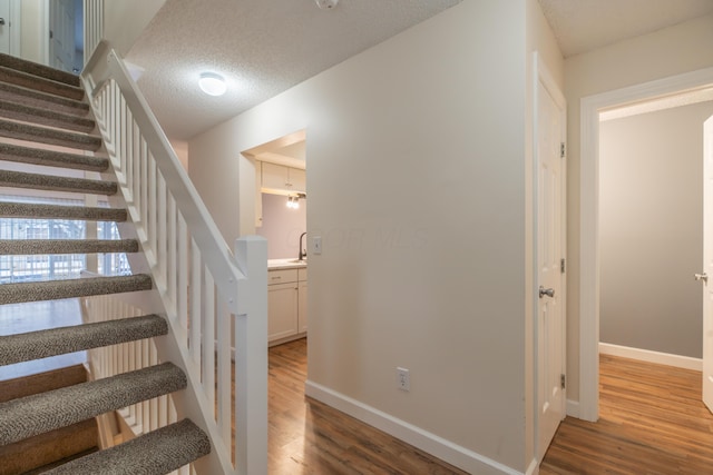 stairs with sink, a textured ceiling, and hardwood / wood-style floors