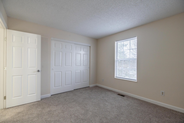 unfurnished bedroom featuring light colored carpet, a textured ceiling, and a closet