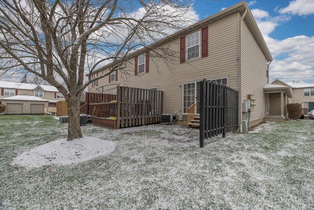 snow covered house featuring a garage, central AC unit, and a lawn