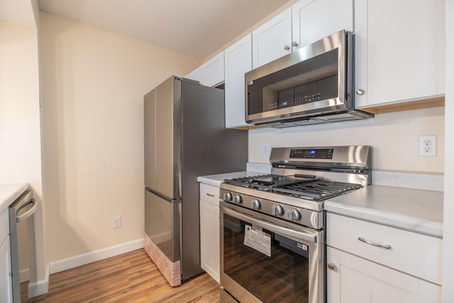 kitchen with a textured ceiling, light hardwood / wood-style floors, white cabinetry, and appliances with stainless steel finishes