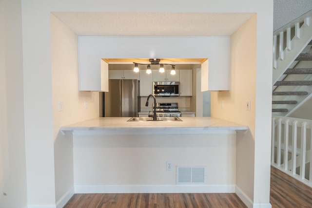 kitchen with sink, stainless steel appliances, kitchen peninsula, and dark hardwood / wood-style flooring