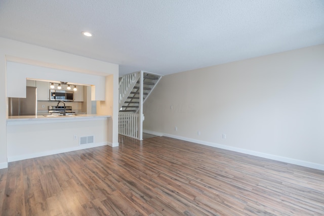 unfurnished living room featuring wood-type flooring, sink, and a textured ceiling