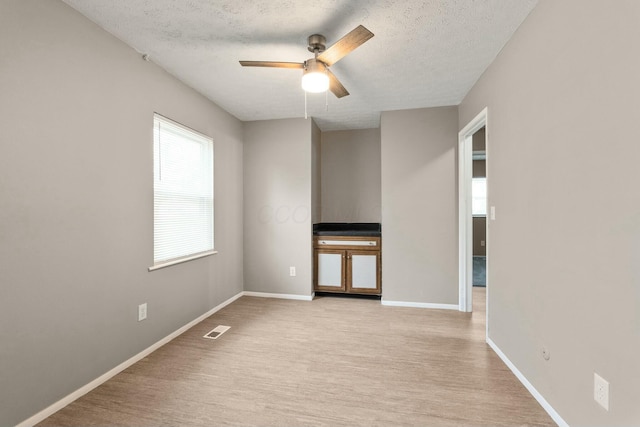 spare room with ceiling fan, light hardwood / wood-style flooring, and a textured ceiling