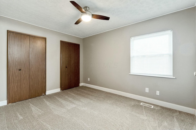 unfurnished bedroom featuring carpet flooring, multiple closets, ceiling fan, and a textured ceiling