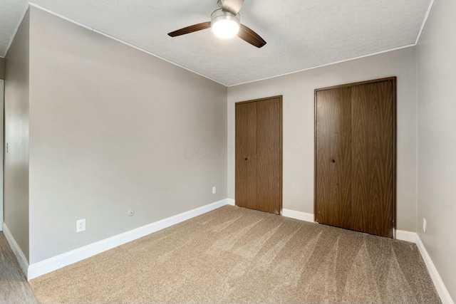 unfurnished bedroom featuring carpet flooring, ceiling fan, a textured ceiling, and two closets