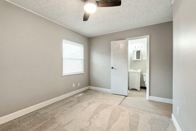 unfurnished bedroom with connected bathroom, ceiling fan, light carpet, and a textured ceiling