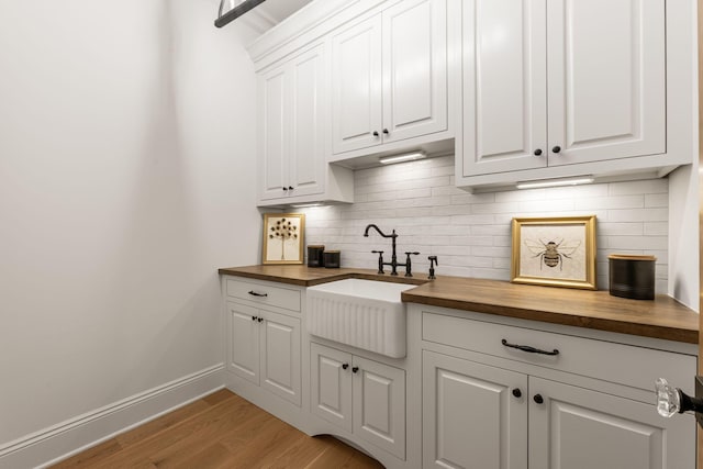 bar featuring light wood-type flooring, baseboards, decorative backsplash, and a sink