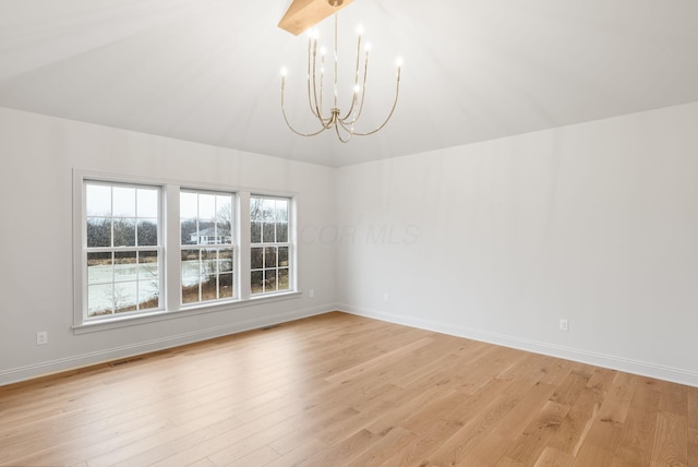 empty room with lofted ceiling, light wood finished floors, a chandelier, and baseboards