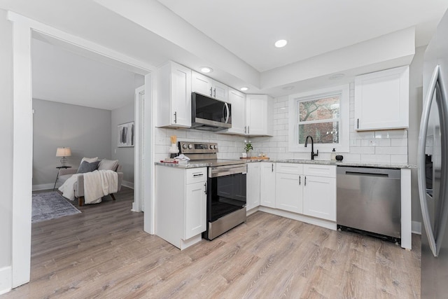 kitchen featuring stainless steel appliances, white cabinetry, light hardwood / wood-style floors, and light stone counters