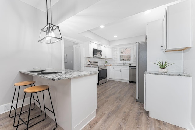 kitchen with white cabinetry, light stone counters, kitchen peninsula, decorative light fixtures, and appliances with stainless steel finishes