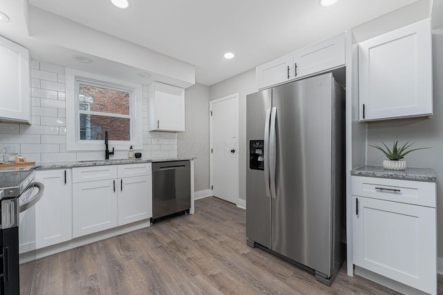 kitchen featuring white cabinetry, sink, light stone counters, hardwood / wood-style floors, and appliances with stainless steel finishes