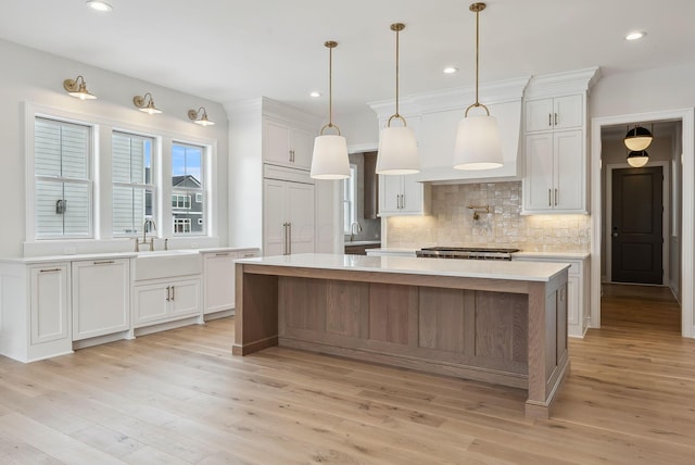 kitchen featuring tasteful backsplash, white cabinetry, hanging light fixtures, light wood-type flooring, and a kitchen island