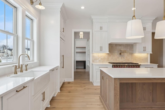 kitchen with decorative light fixtures, sink, white cabinetry, and custom range hood