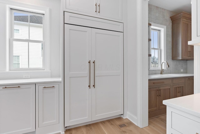 kitchen with light wood-type flooring, decorative backsplash, and white cabinetry