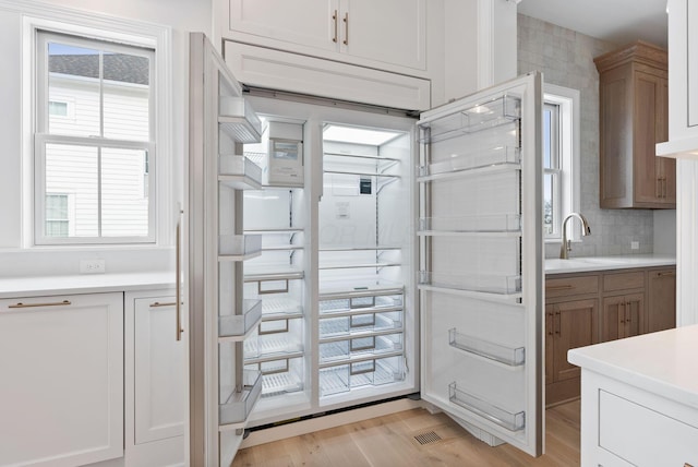 kitchen with light wood-type flooring, decorative backsplash, fridge, and white cabinetry