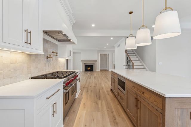 kitchen with custom exhaust hood, appliances with stainless steel finishes, white cabinets, decorative light fixtures, and backsplash