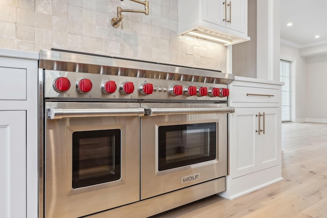 kitchen with white cabinetry, decorative backsplash, range with two ovens, and crown molding