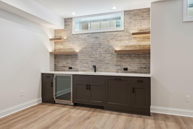 bar featuring light hardwood / wood-style floors, tasteful backsplash, sink, dark brown cabinetry, and wine cooler