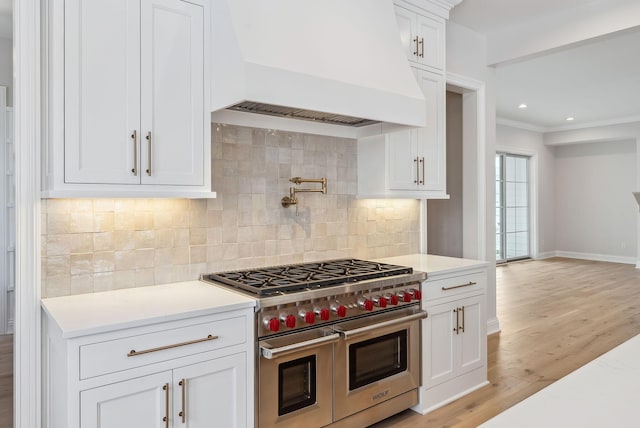 kitchen with tasteful backsplash, white cabinetry, custom range hood, light wood-type flooring, and range with two ovens