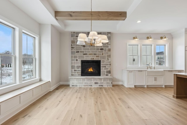 unfurnished living room with sink, plenty of natural light, beamed ceiling, and light wood-type flooring