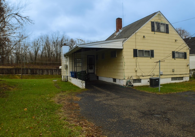 rear view of property featuring a carport, a yard, and central AC