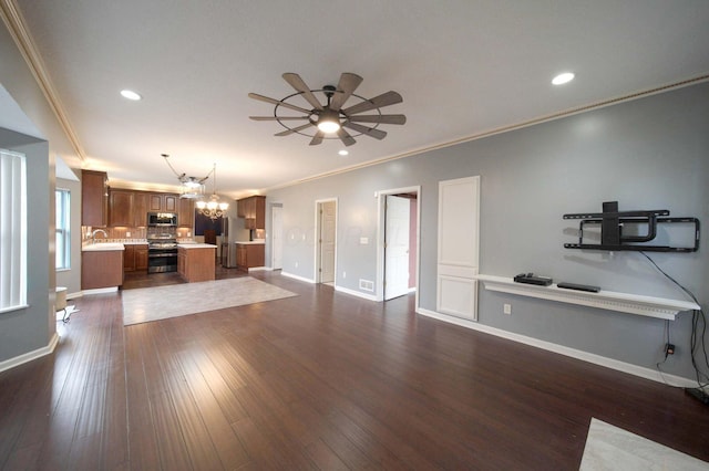 unfurnished living room featuring baseboards, ornamental molding, dark wood-type flooring, a sink, and recessed lighting