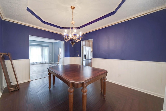 unfurnished dining area with a tray ceiling, a wainscoted wall, crown molding, a notable chandelier, and a textured ceiling